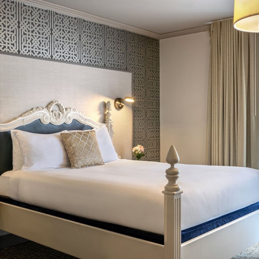 Classic bed by tan curtains and a geometric wall under soft lighting in Balcony Suite at Warwick San Francisco