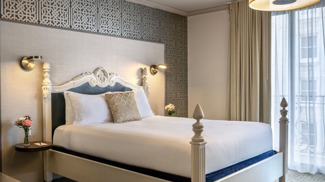 Classic bed by tan curtains and a geometric wall under soft lighting in Balcony Suite at Warwick San Francisco