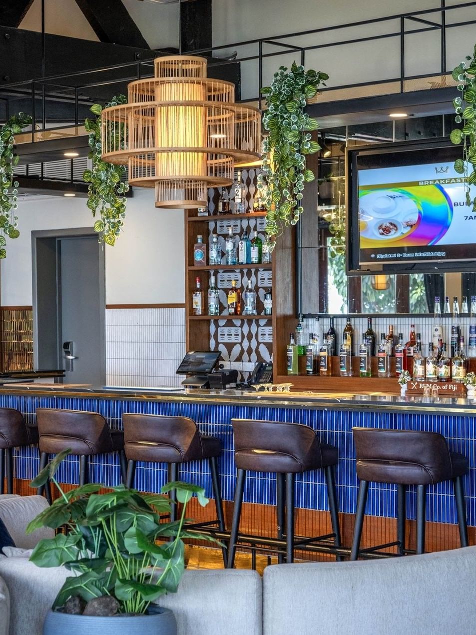 Brown bar stools by a blue tiled counter under hanging vines and lights in Hibiscus Lounge at Warwick Fiji Resort and Spa