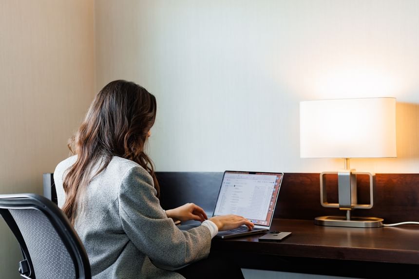 Woman working at a desk with a laptop and lamp, highlighting cozy places to stay in Charlottetown at Rodd Royalty