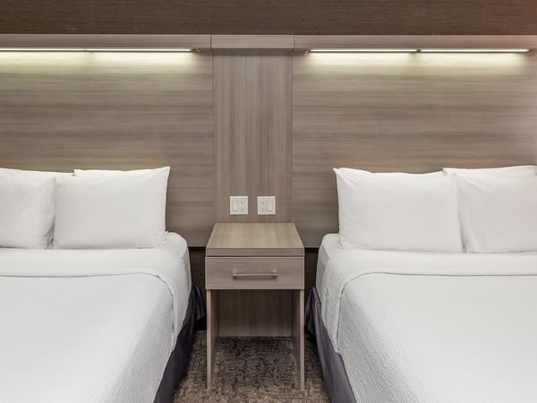Coast Two Queens room with two queen beds, modern wood headboards, and nightstand at Coast Calgary University Area Hotel by APA.