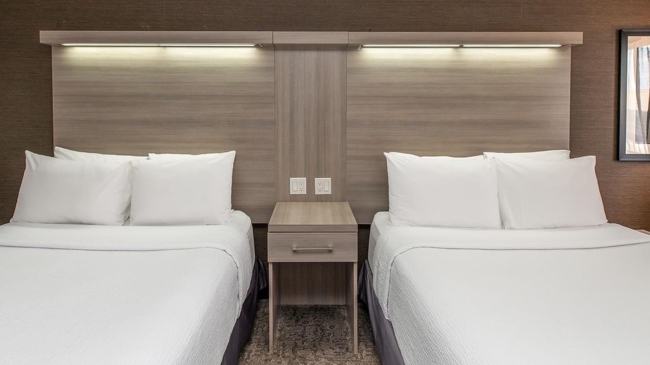 Coast Two Queens room with two queen beds, modern wood headboards, and nightstand at Coast Calgary University Area Hotel by APA.