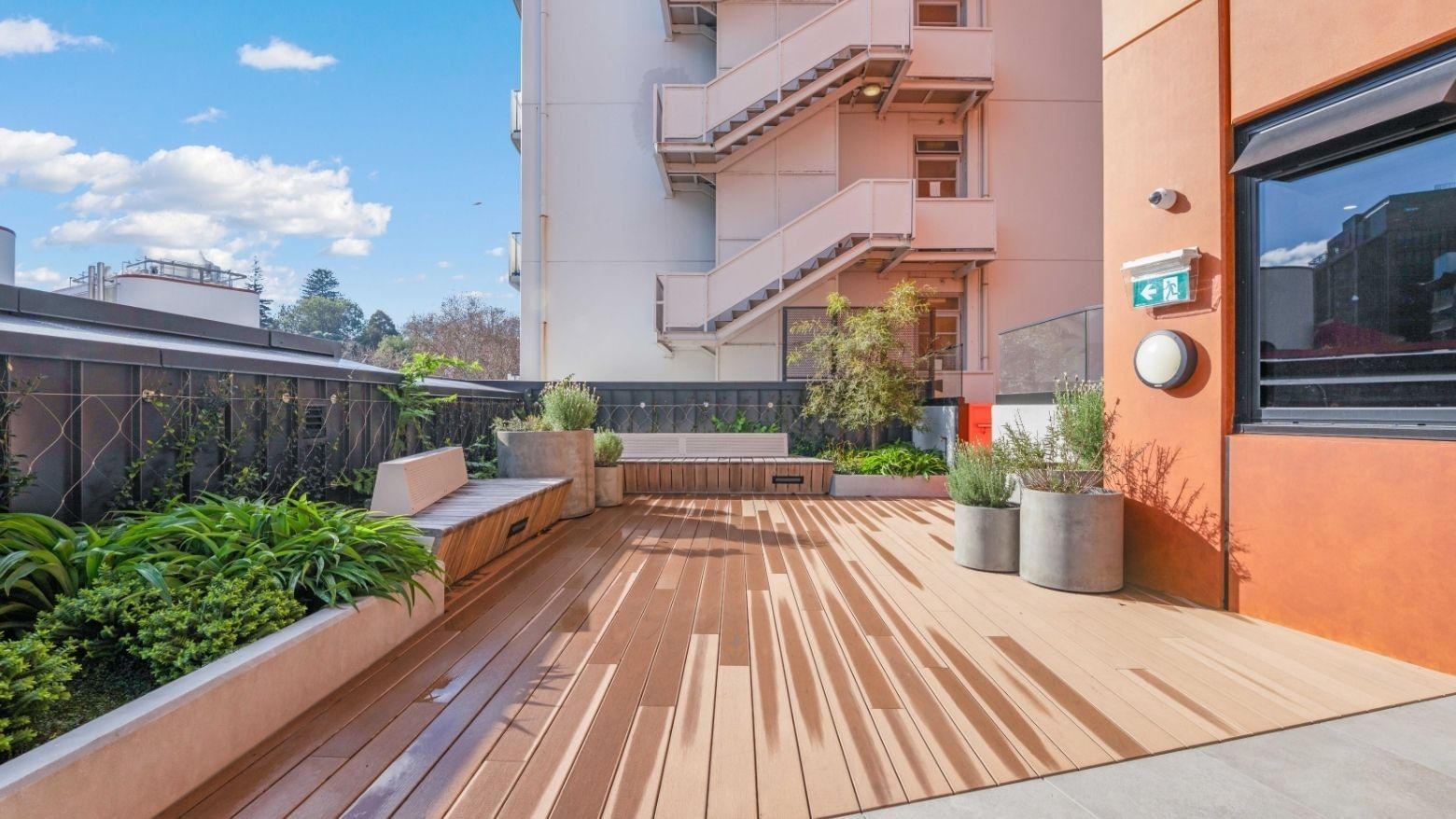 Rooftop terrace with wooden decking, built-in seating, planters, and city views at UniLodge Auckland Central.