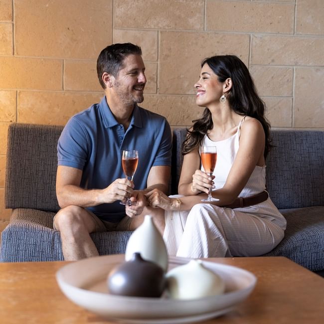 Couple enjoying wine and chocolates on a sofa in a modern lounge setting for a Romantic Escapes Package