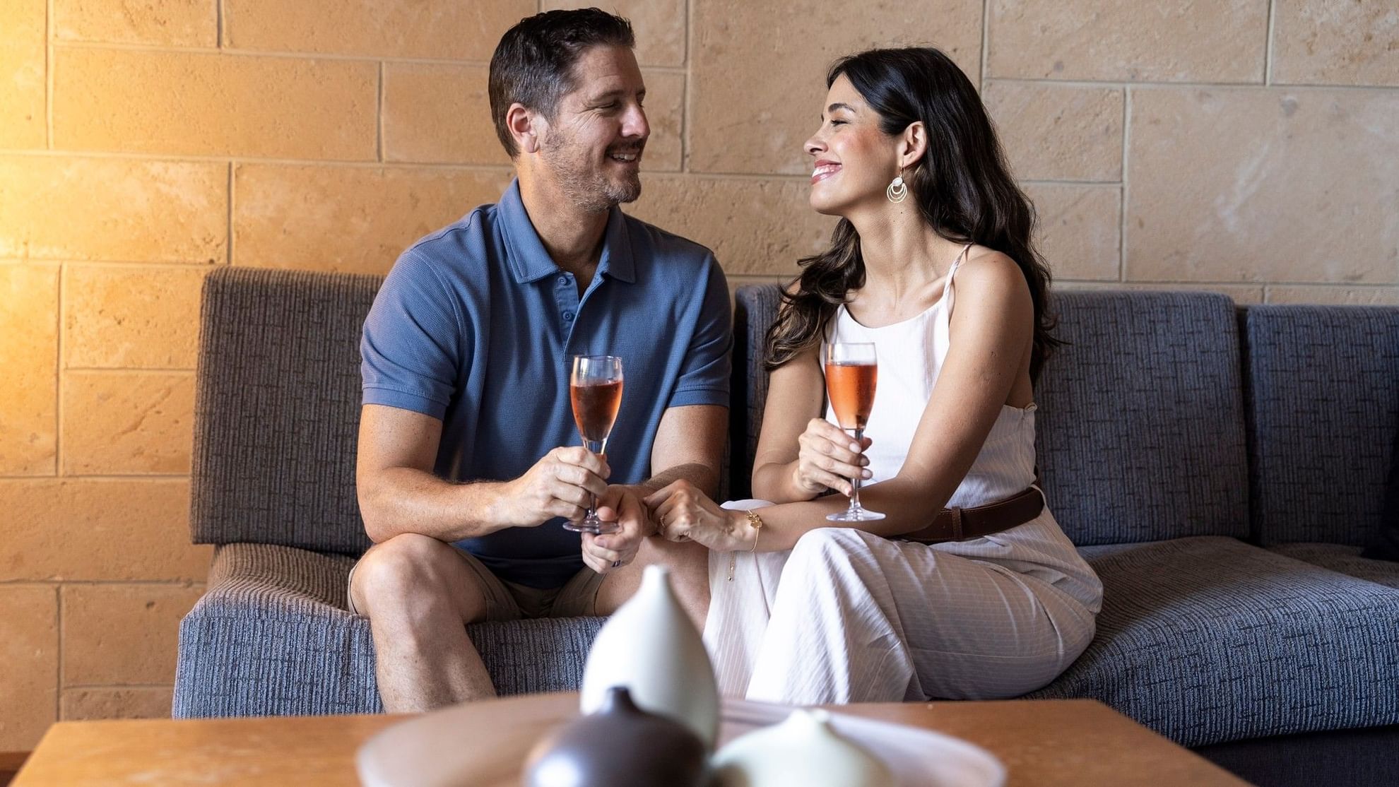 Couple enjoying wine and chocolates on a sofa in a modern lounge setting for a Romantic Escapes Package