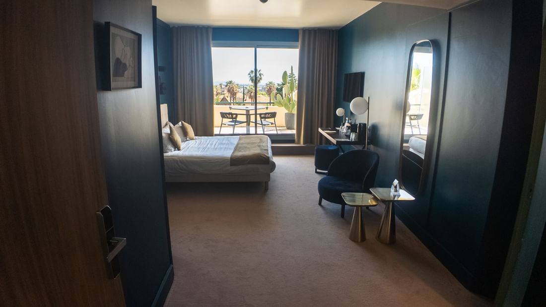 Chambre d'hôtel avec lit, fauteuil, table, balcon et vue sur la mer.