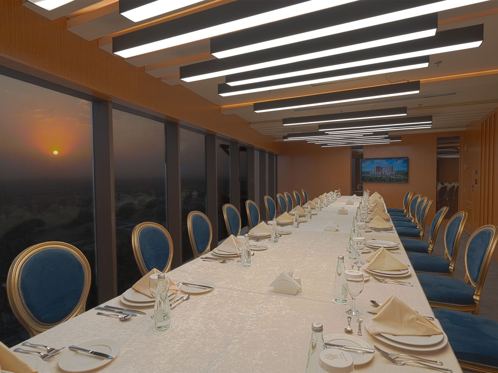 Long dining table set for a formal dinner with large windows showing the sunset at World Heart Hotel Baghdad.