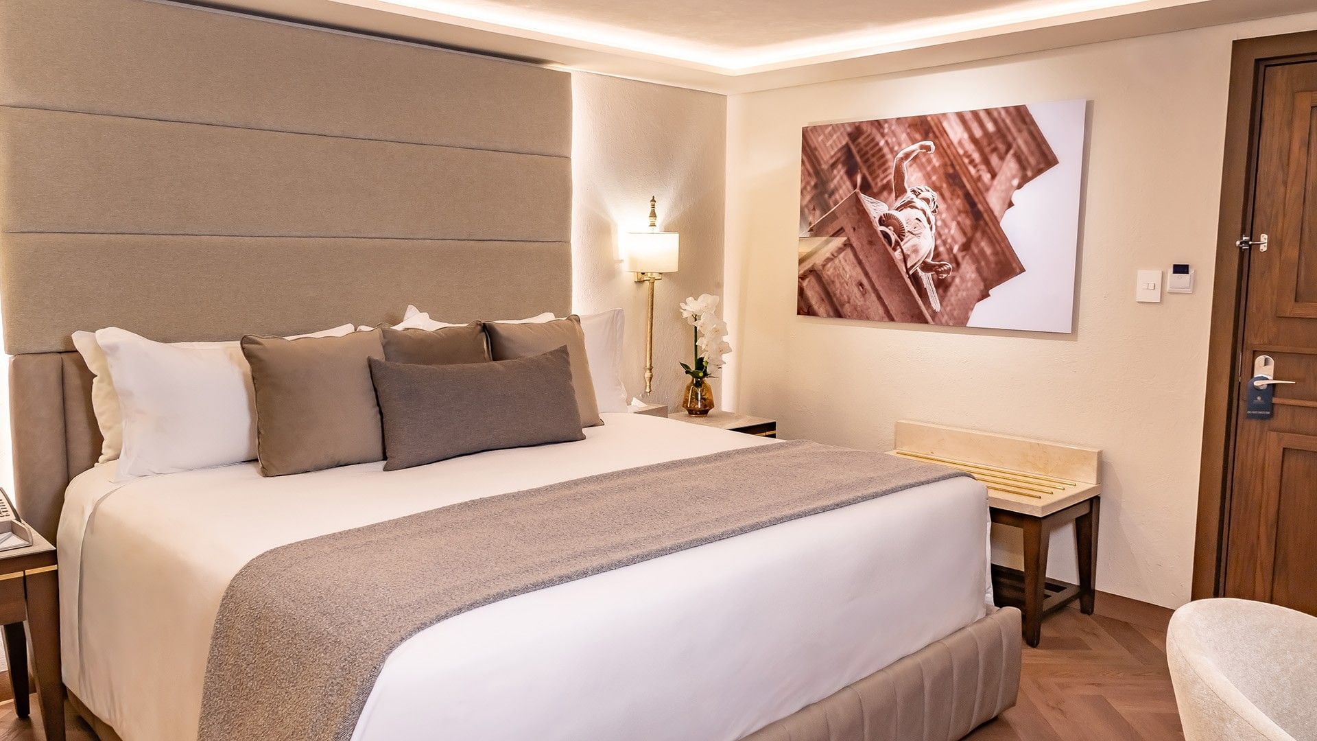 Queen New Class cozy bed with neutral-toned pillows, a grey runner, and a large framed photo at Quinta Real Puebla