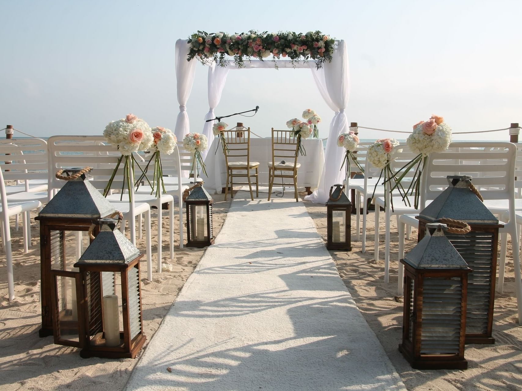 Outdoor wedding ceremony with chairs, lanterns set up, and floral deco in beach at Hotel Isla Del Encanto