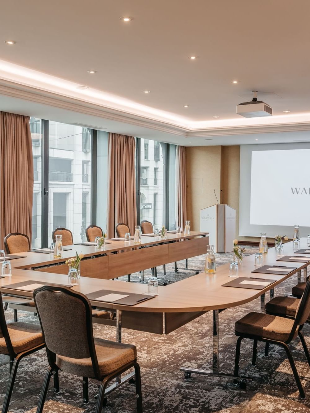 Large u-shaped table with padded chairs under a projector screen in Jura at Warwick Geneva