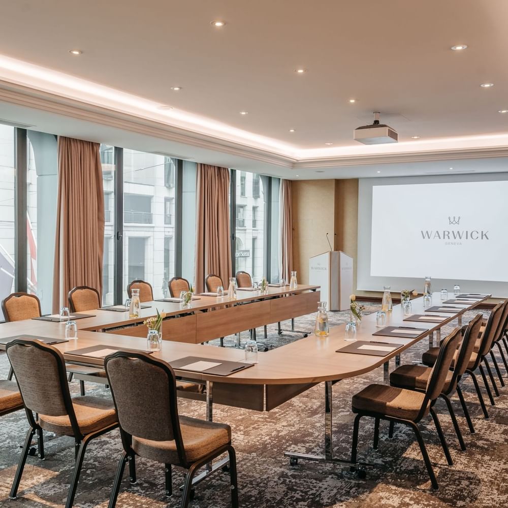 Large u-shaped table with padded chairs under a projector screen in Jura at Warwick Geneva