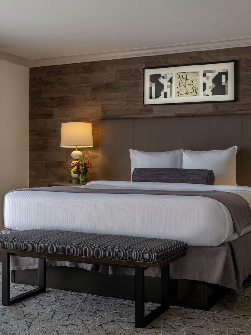 Striped bench by a plush bed under a wood-paneled wall with framed art in Deluxe Room at Warwick Denver