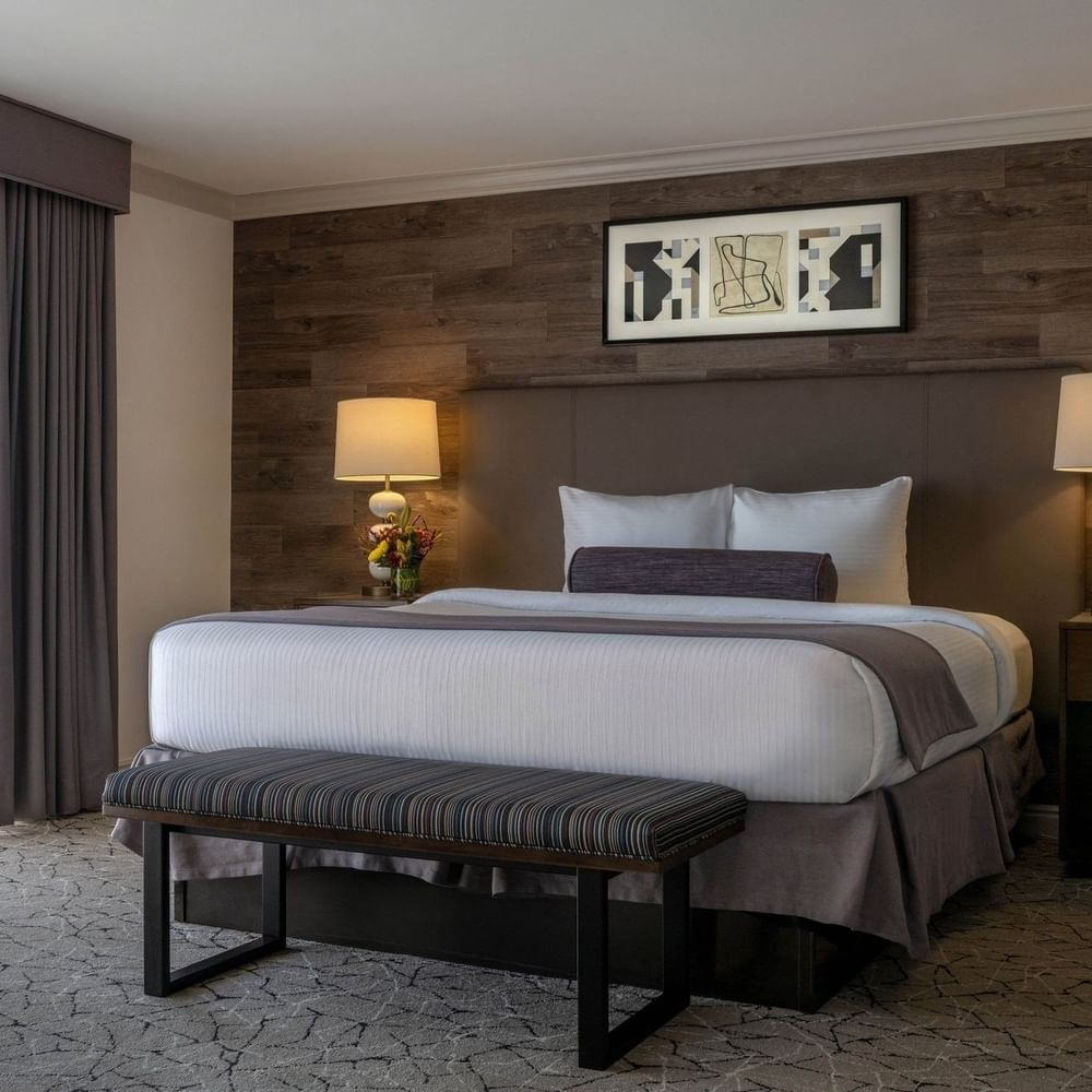 Plush bed with a bolster by a striped bench under warm lamps surrounding a rug in Classic Rooms at Warwick Denver