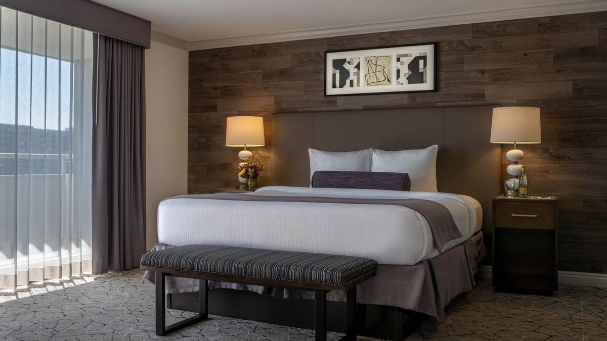 Plush bed with a bolster by a striped bench under warm lamps surrounding a rug in Classic Rooms at Warwick Denver