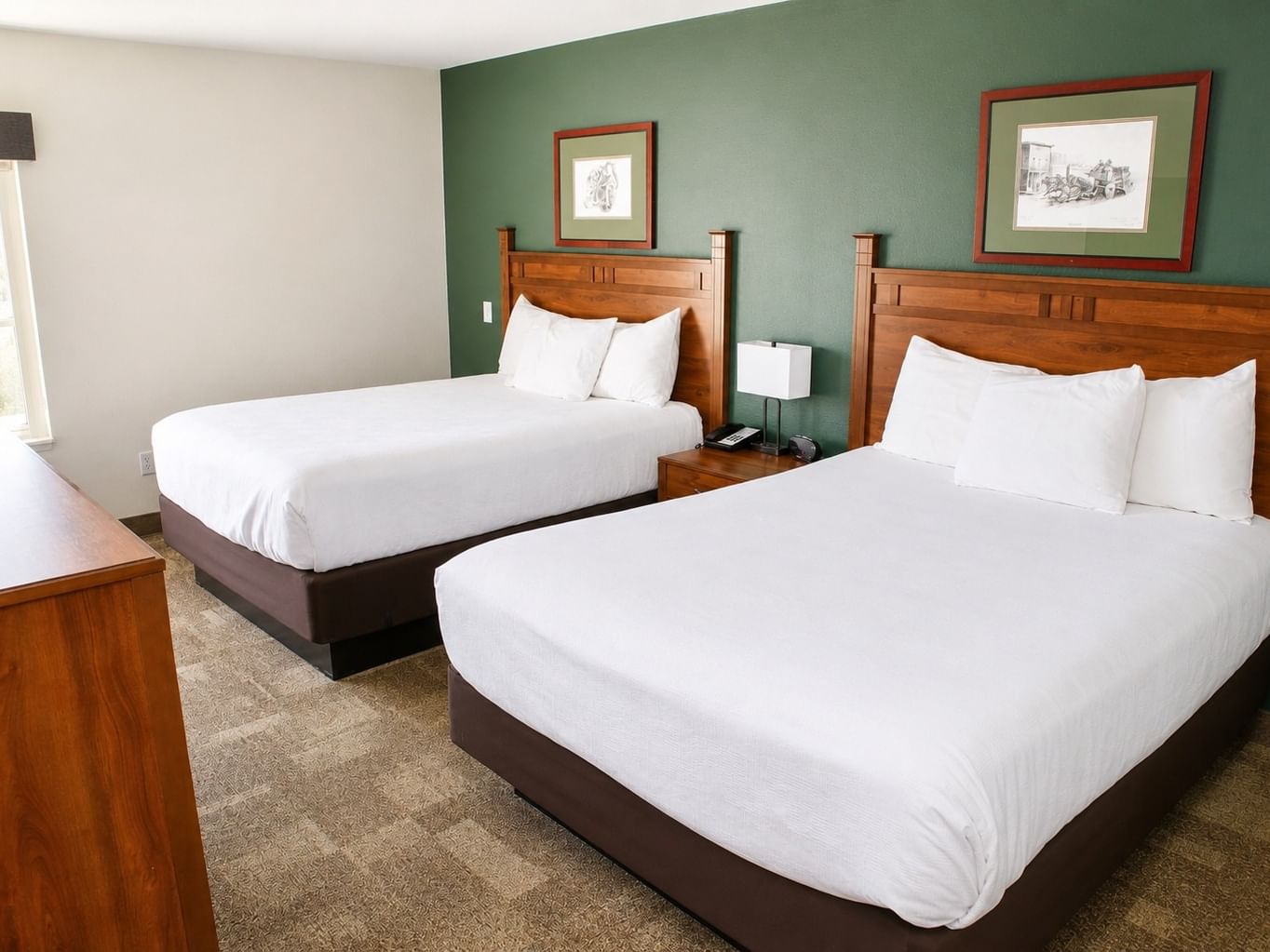 Double Queen room with two queen beds, wooden headboards, white linens, and green accent wall