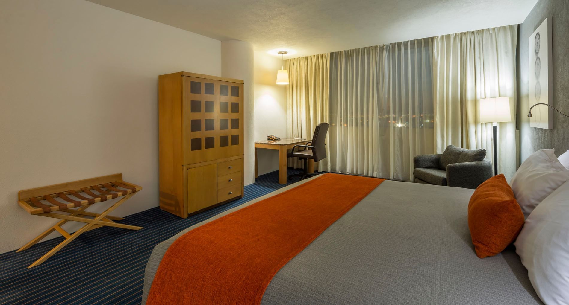 King Deluxe room at Real Inn Nuevo Laredo, featuring a wooden wardrobe, luggage rack, and a dedicated workspace