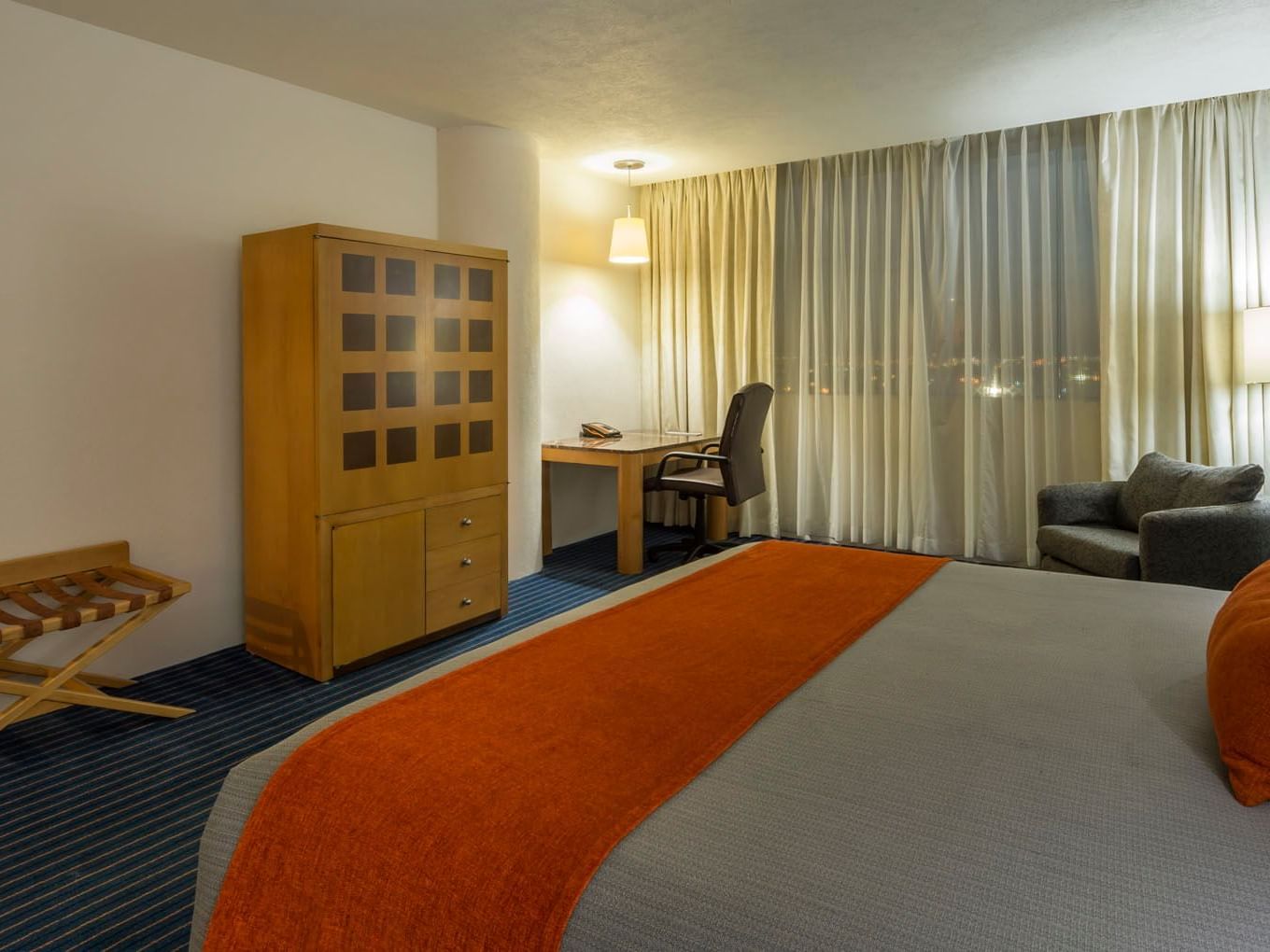 King Deluxe room with a wooden armoire, work desk, and a large bed with an orange runner at Real Inn Nuevo Laredo