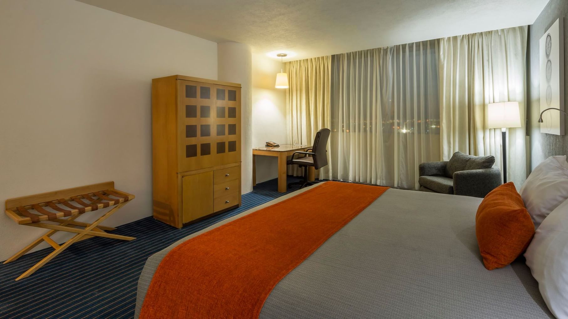 King Deluxe room with a wooden armoire, work desk, and a large bed with an orange runner at Real Inn Nuevo Laredo