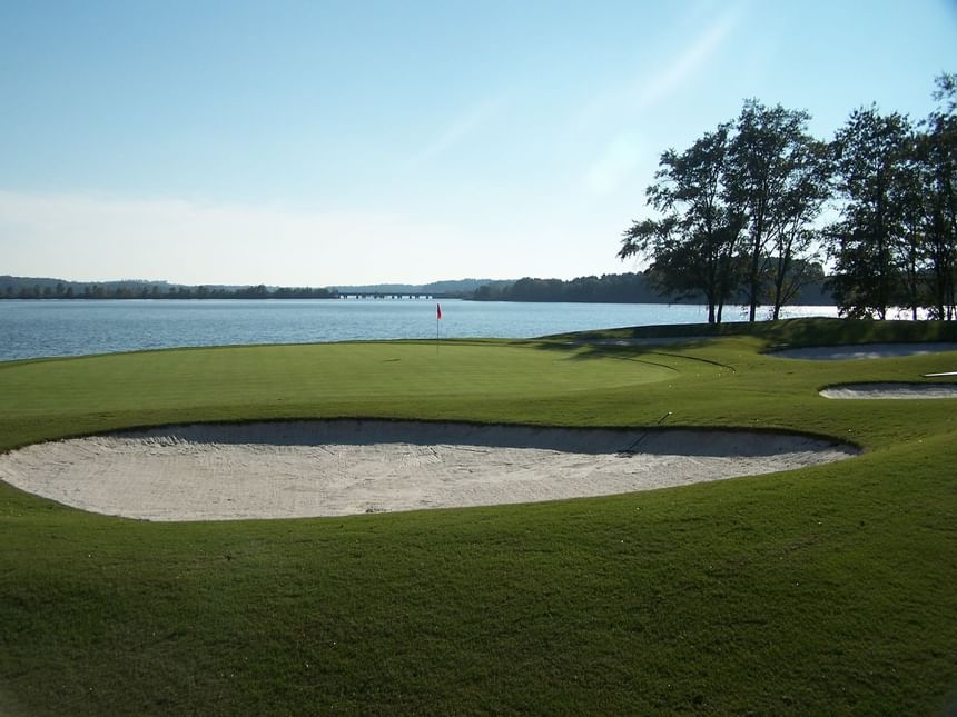 Golf green beside a wide sand bunker overlooking calm blue lake waters at Clemson University Conference Center & Inn