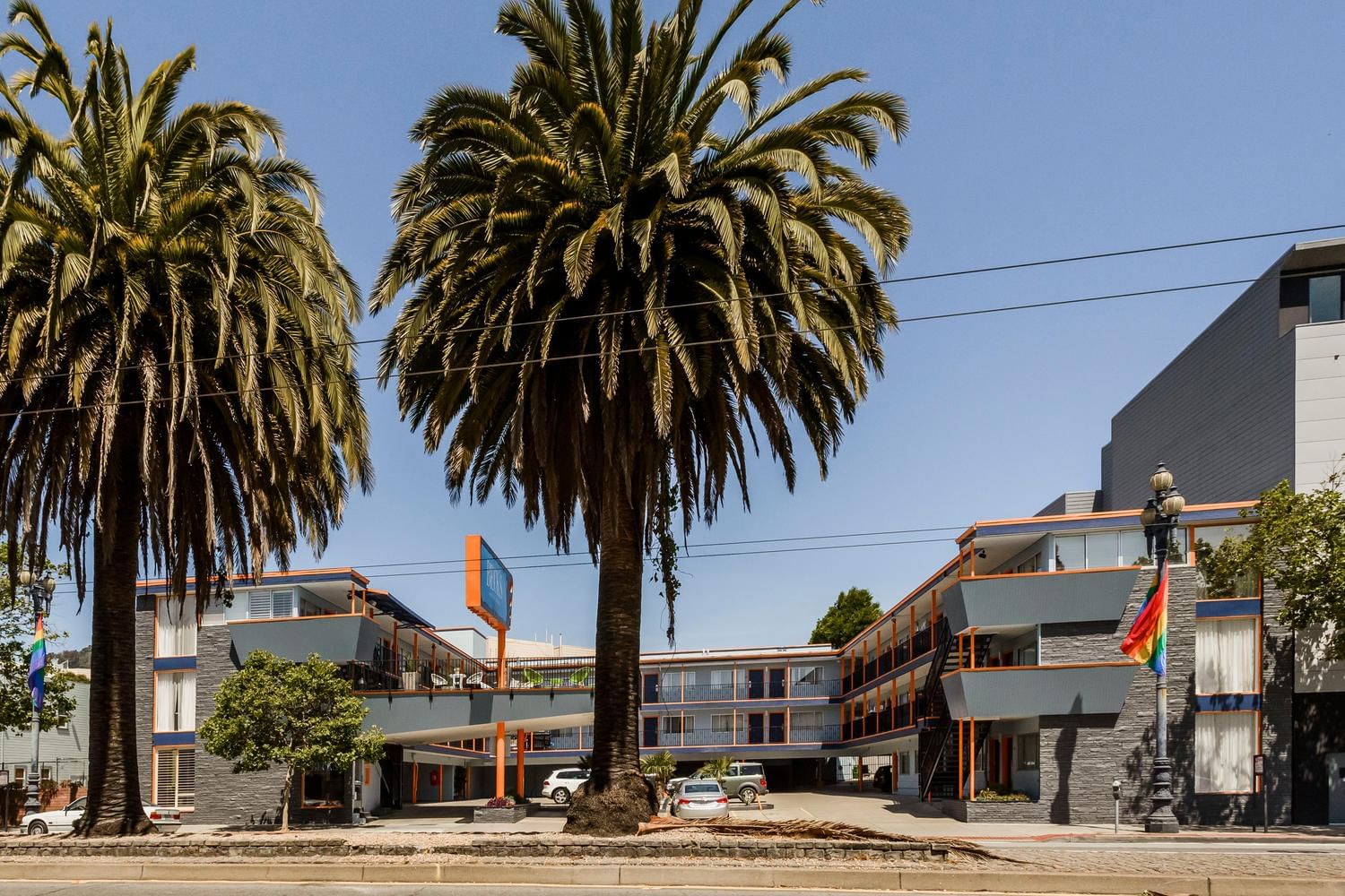 A wide-angle view of a multi-story building with a parking lot and palm trees in front of it.