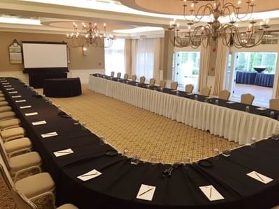 U-shaped conference setup with long tables covered in black cloth and a projector screen at The Simsbury Inn 
