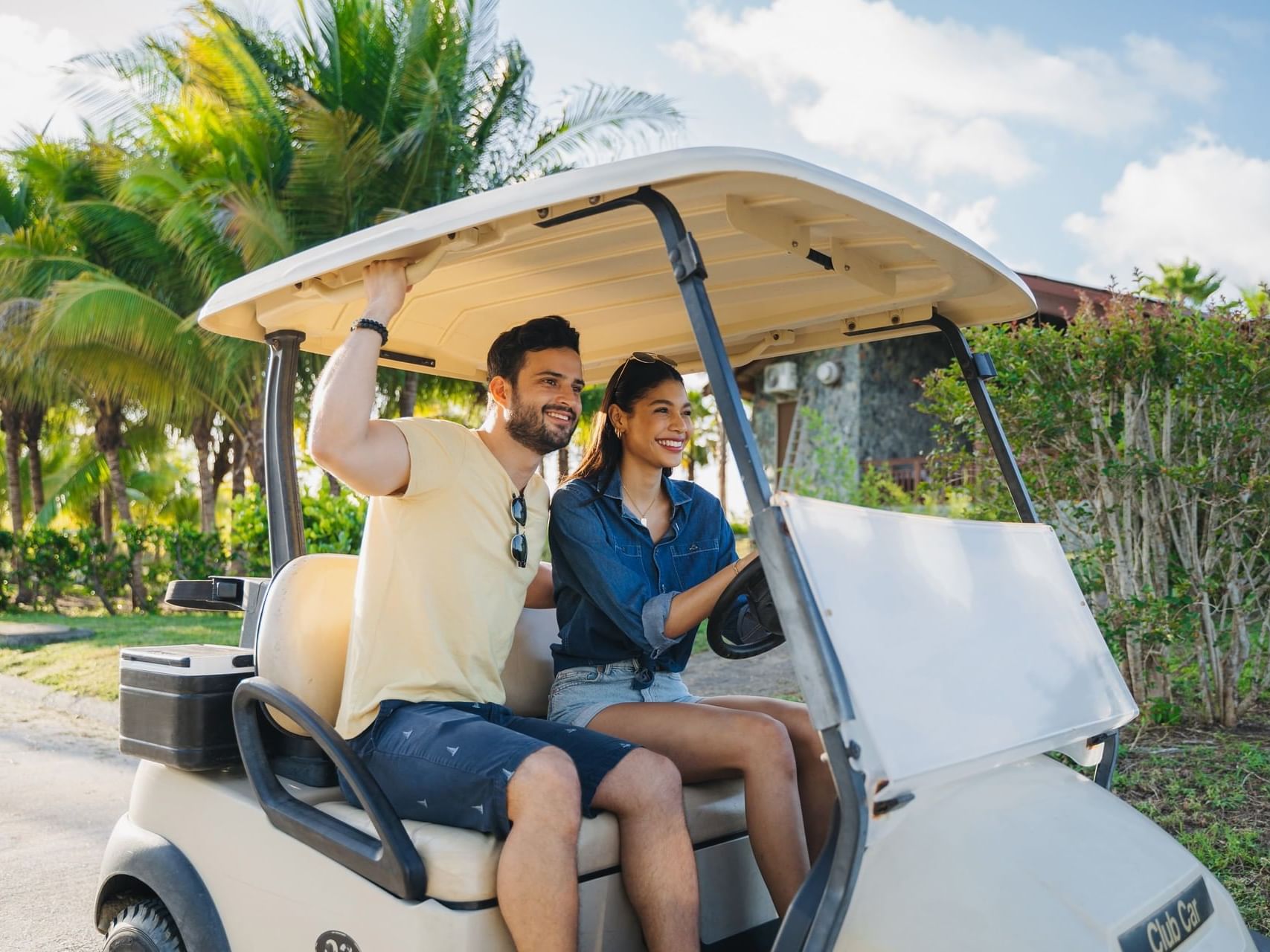 Couple riding a golf cart outdoors with tropical vegetation backdrop at Indura Beach & Golf Resort