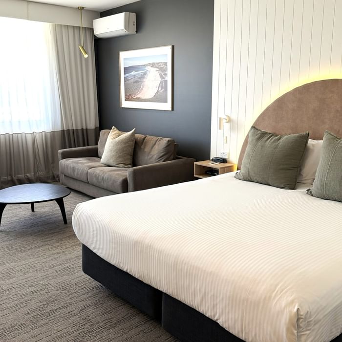 Comfortable room with a large bed, couch, and beach artwork at Mercure Charlestown.