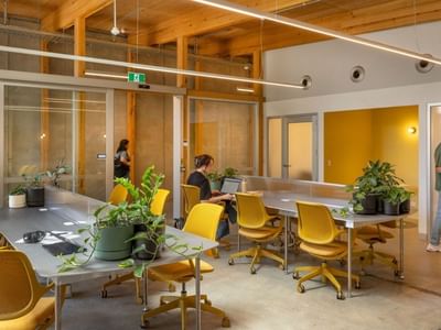 Modern coworking space with yellow chairs, wooden beams, glass partitions, and people working at Swift Walk.