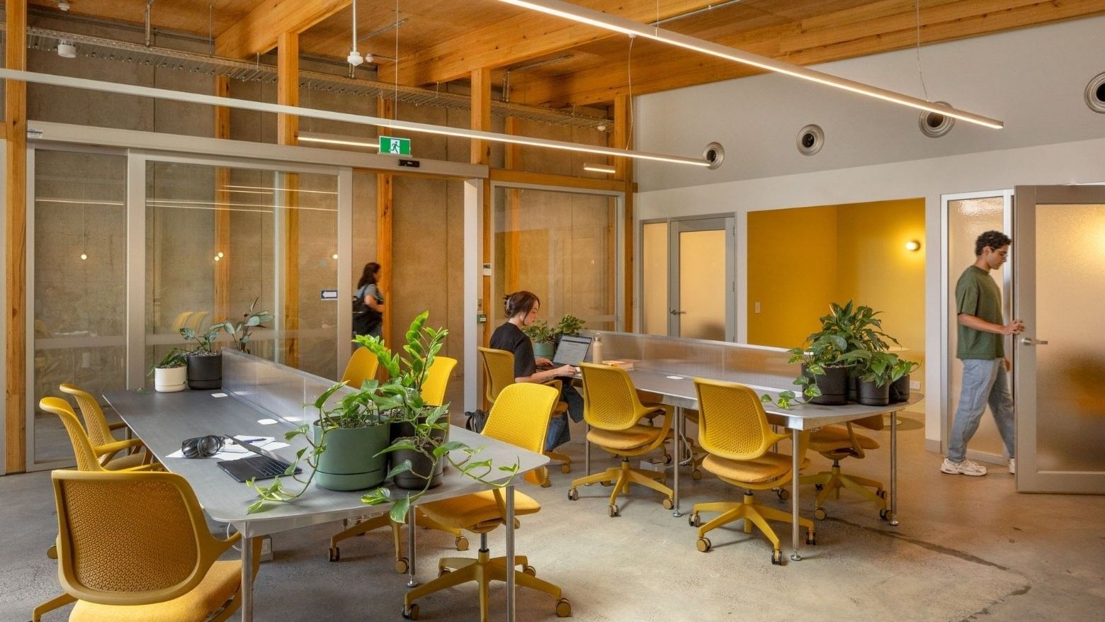 Modern coworking space with yellow chairs, wooden beams, glass partitions, and people working at Swift Walk.