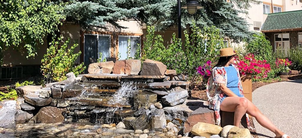 Woman relaxing by a waterfall feature in a garden at Coast Canmore Hotel.