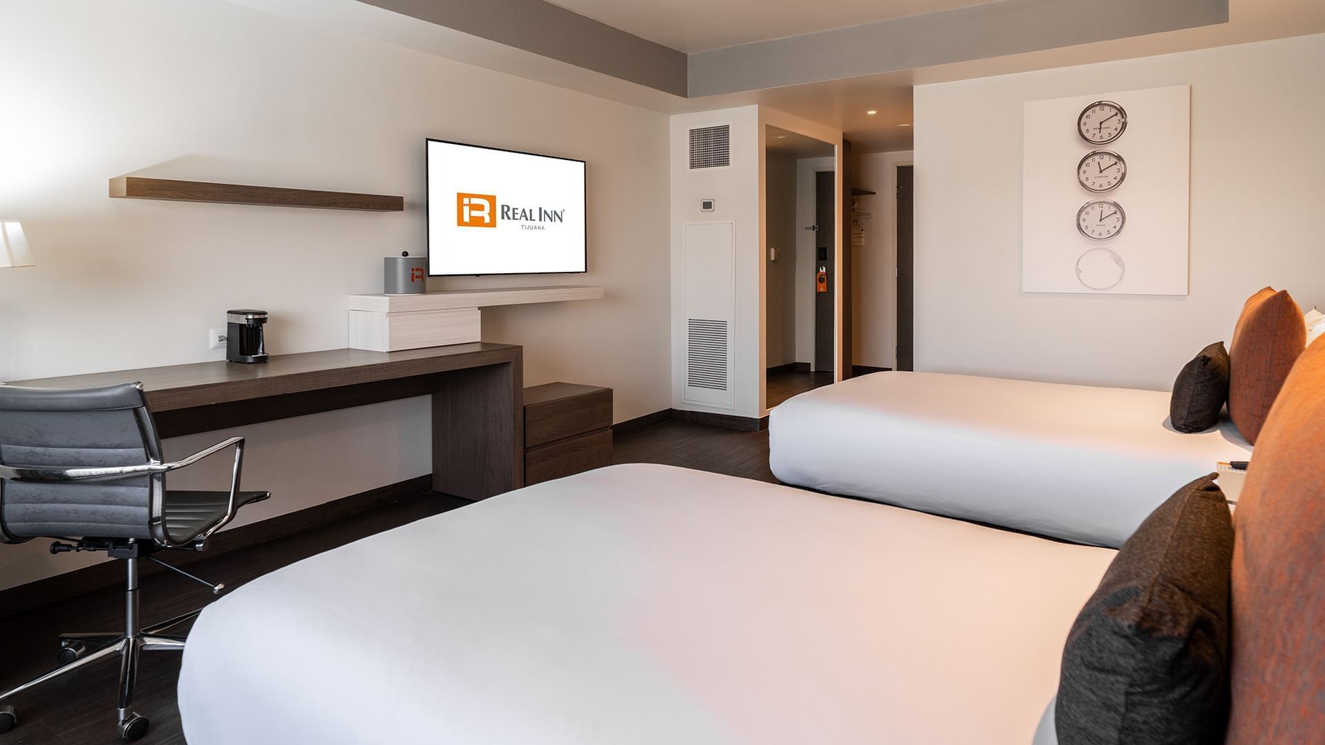 Wall-mounted TV, coffee maker, and work desk facing the bed in the Two Double Deluxe Room at the Real Inn Tijuana