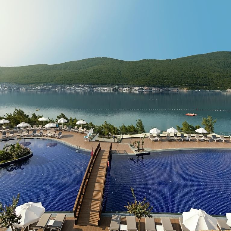 Просторный главный бассейн в Titanic Luxury Collection Bodrum с шезлонгами и зонтиками.