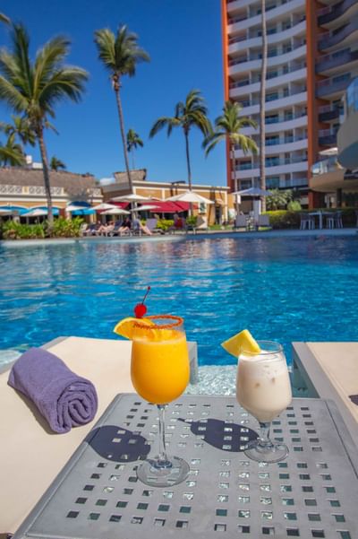 Dos cócteles vibrantes sobre una mesa entre dos tumbonas, junto a la piscina del Sunset Plaza Beach Resort, uno de los mejores hoteles con vistas a la playa en Puerto Vallarta