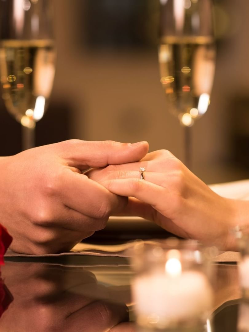 Hands by a red rose under champagne glasses near glowing candles at Warwick Denver