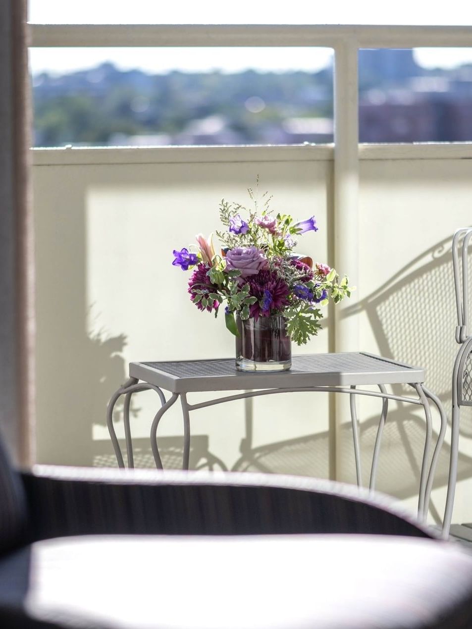 Flowers on a table by a white chair on a sunny balcony in Premier Junior Suites at Warwick Denver