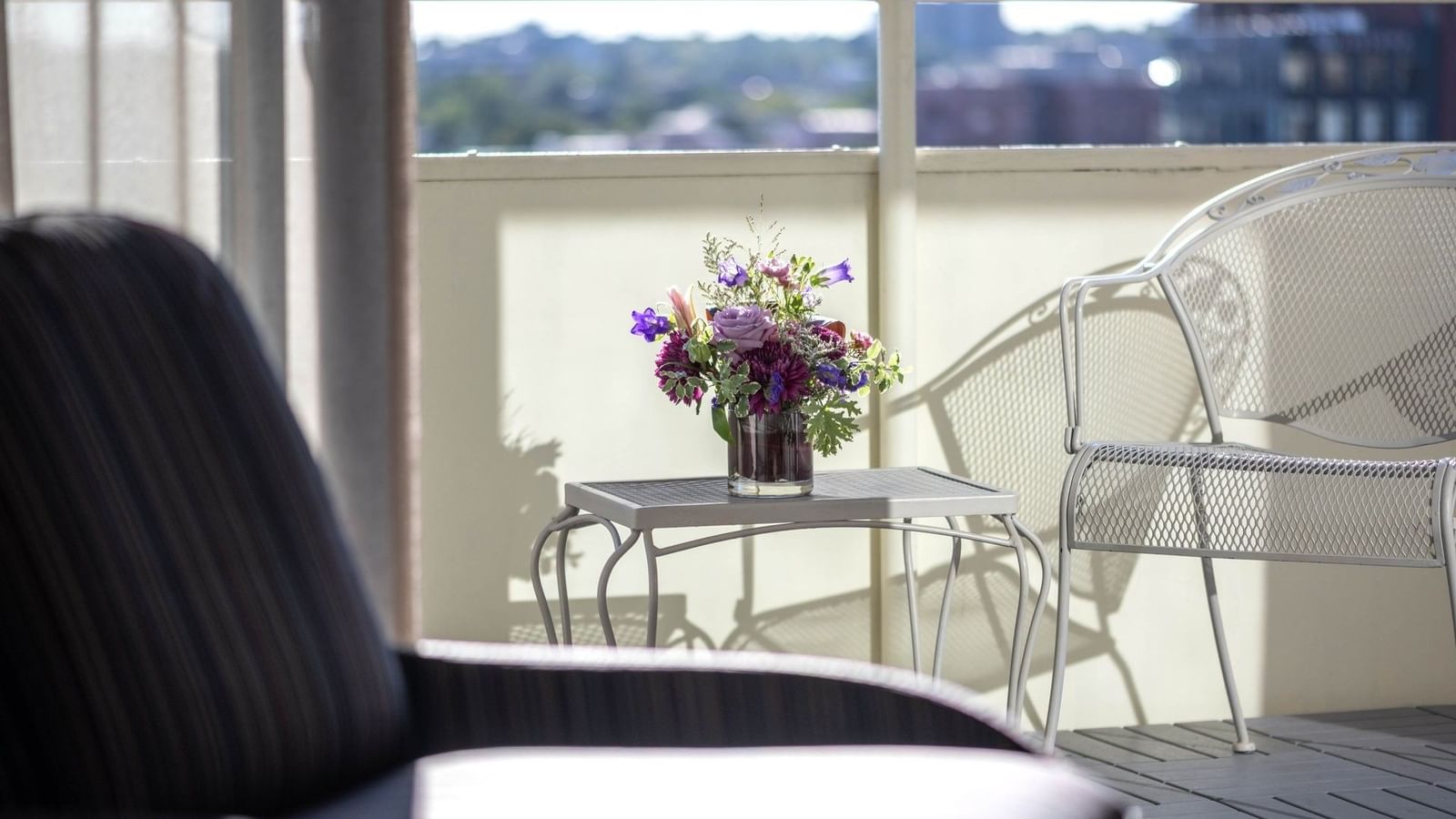 Flowers on a table by a white chair on a sunny balcony in Premier Junior Suites at Warwick Denver