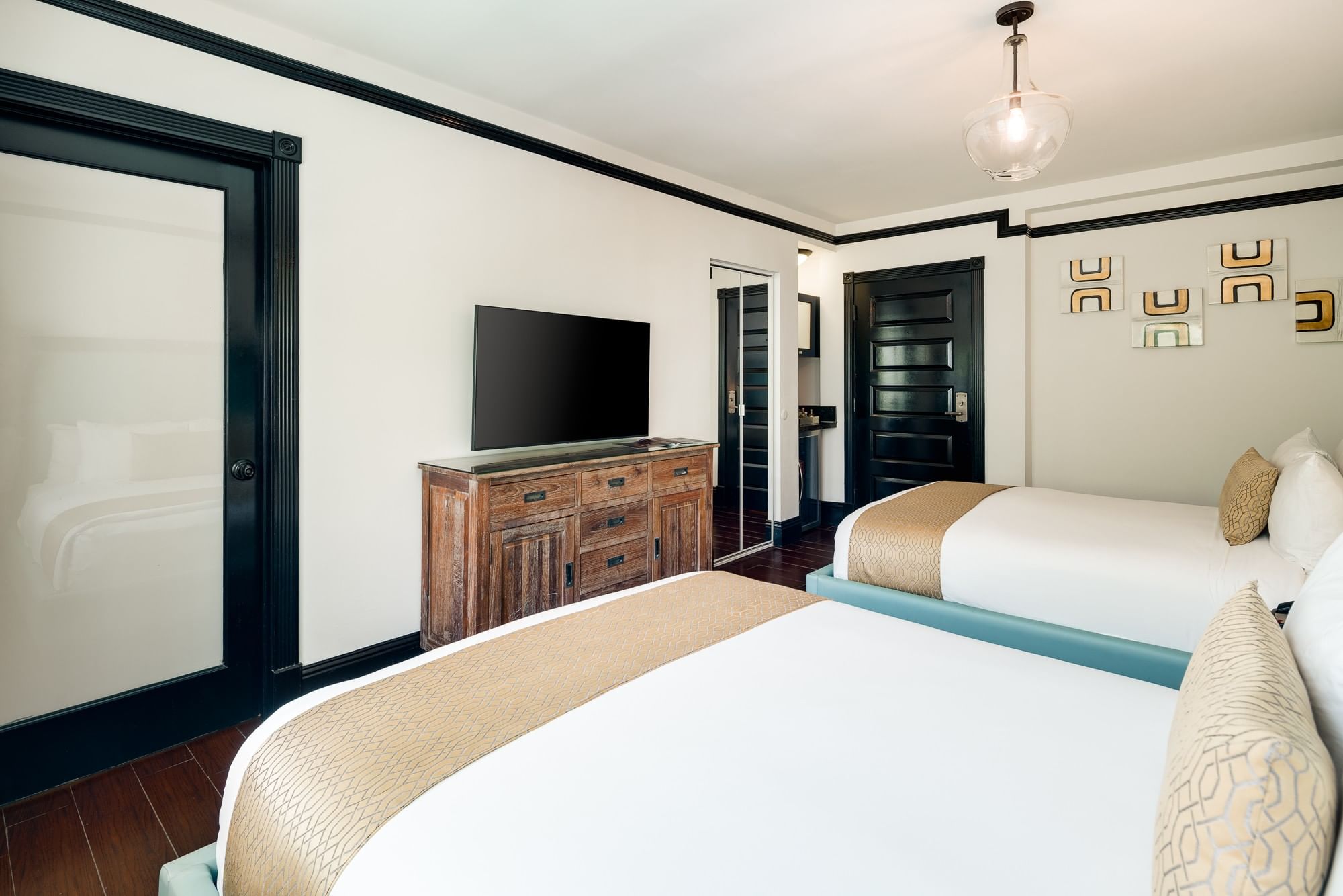 A hotel room with two beds, a TV on a dresser, and a door leading to another room.