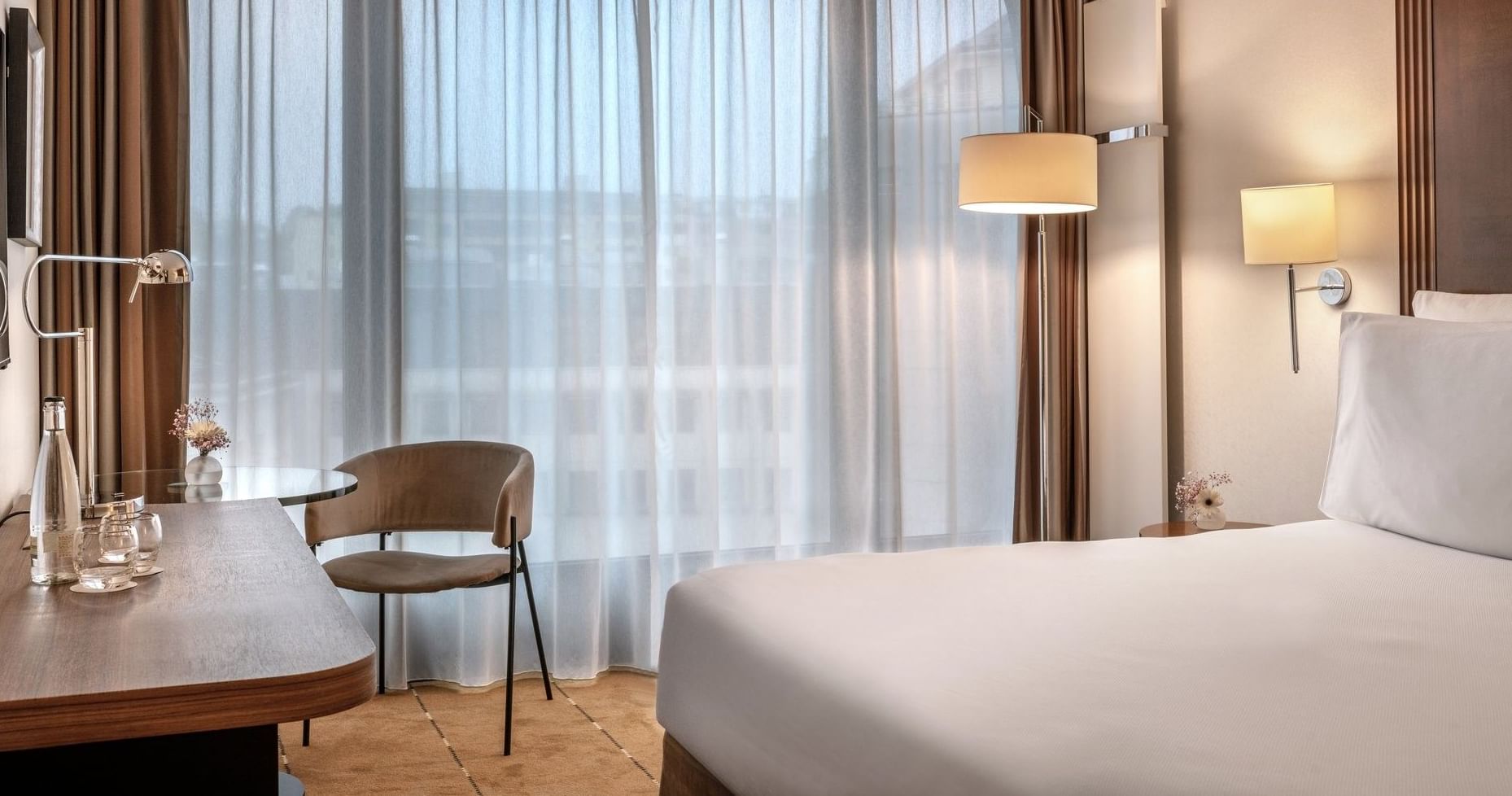 Modern chair by a desk under glowing lamps surrounding a white bed in Superior Room at Warwick Geneva