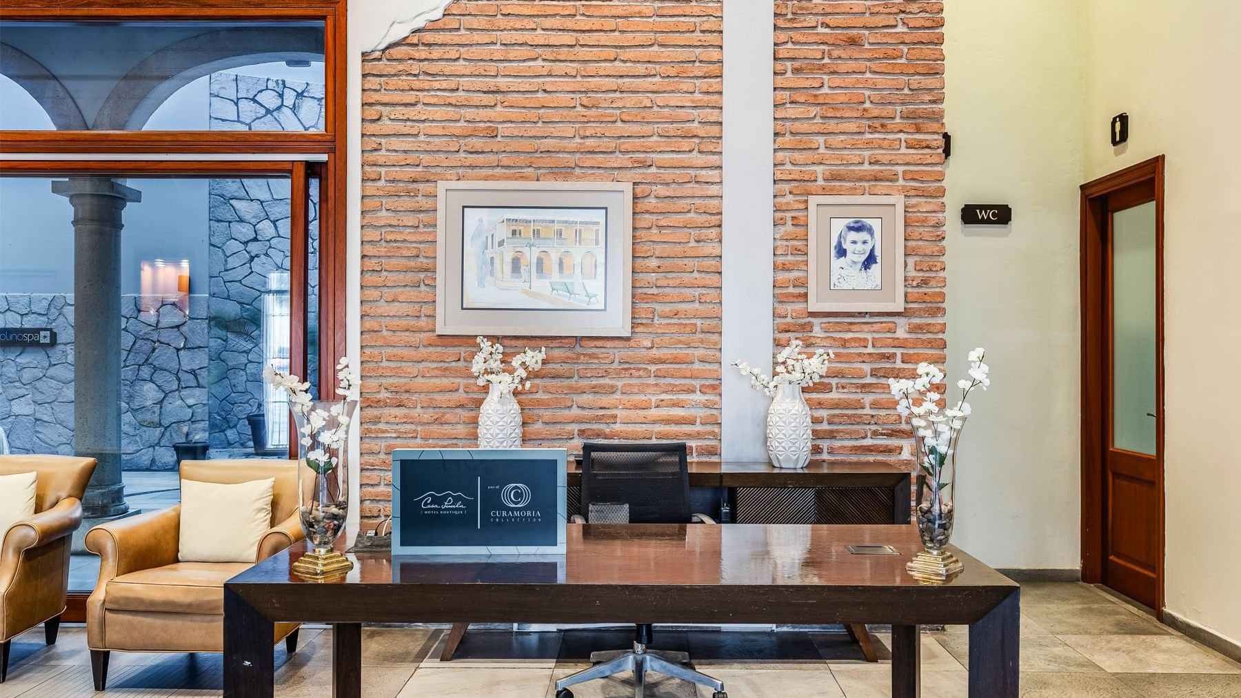 Elegant lobby featuring a wooden desk, brick accent wall, and classic decor at Curamoria Collection