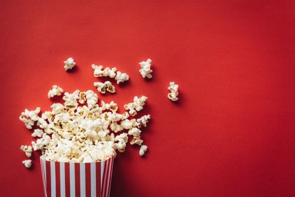 A spilled striped popcorn container against a red background.
