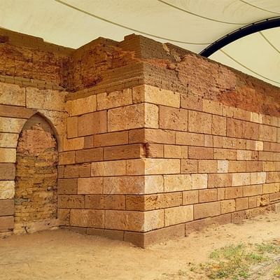 Ruinöse Steinmauer mit Torbogen unter einer weißen Schutzabdeckung in einer ländlichen Umgebung.