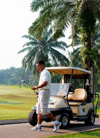 Golfer walking beside a cart on a lush, palm-lined course on a sunny day near The Saujana Hotel Kuala Lumpur