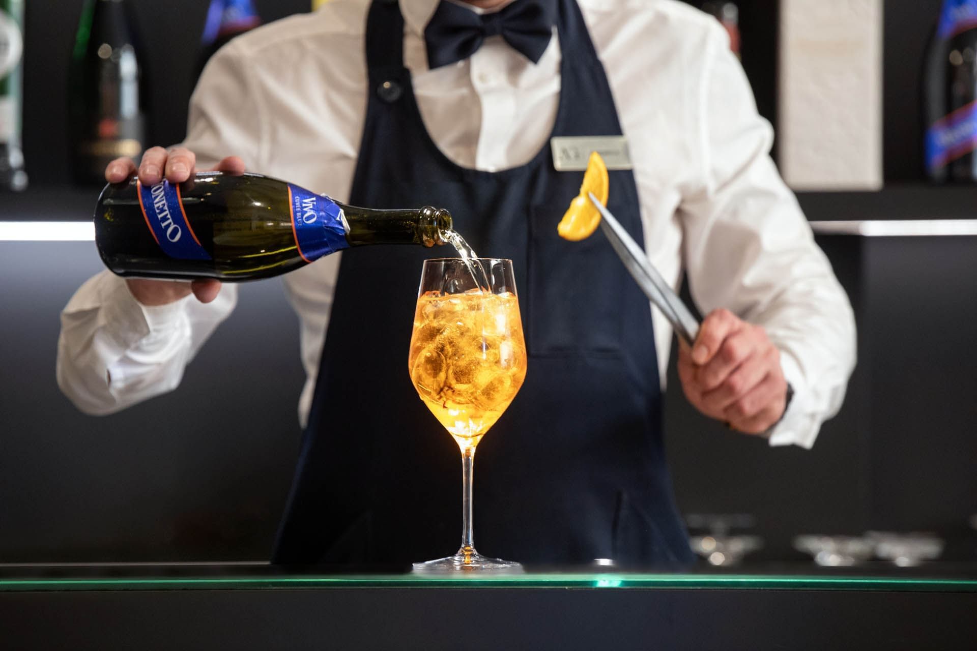 Bartender in a bow tie pours sparkling wine into a glass while garnishing it with an orange slice at The Republic Hotel