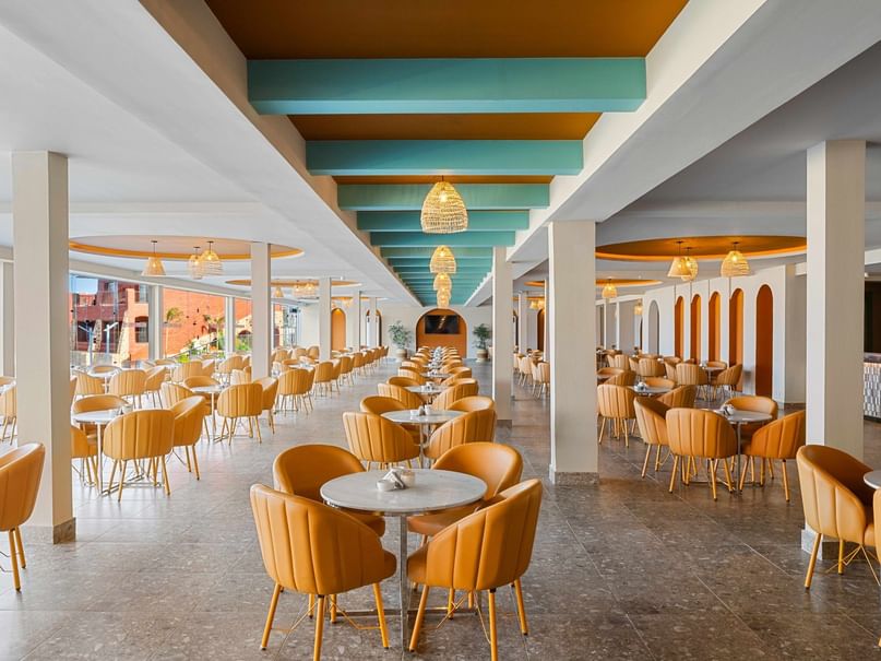 A large dining area with rows of tables and chairs, colorful decor, and pendant lights hanging from the ceiling.