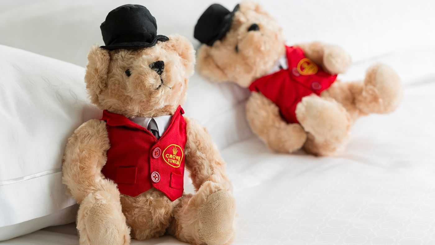 Two teddy bears on a bed at Crown Hotels