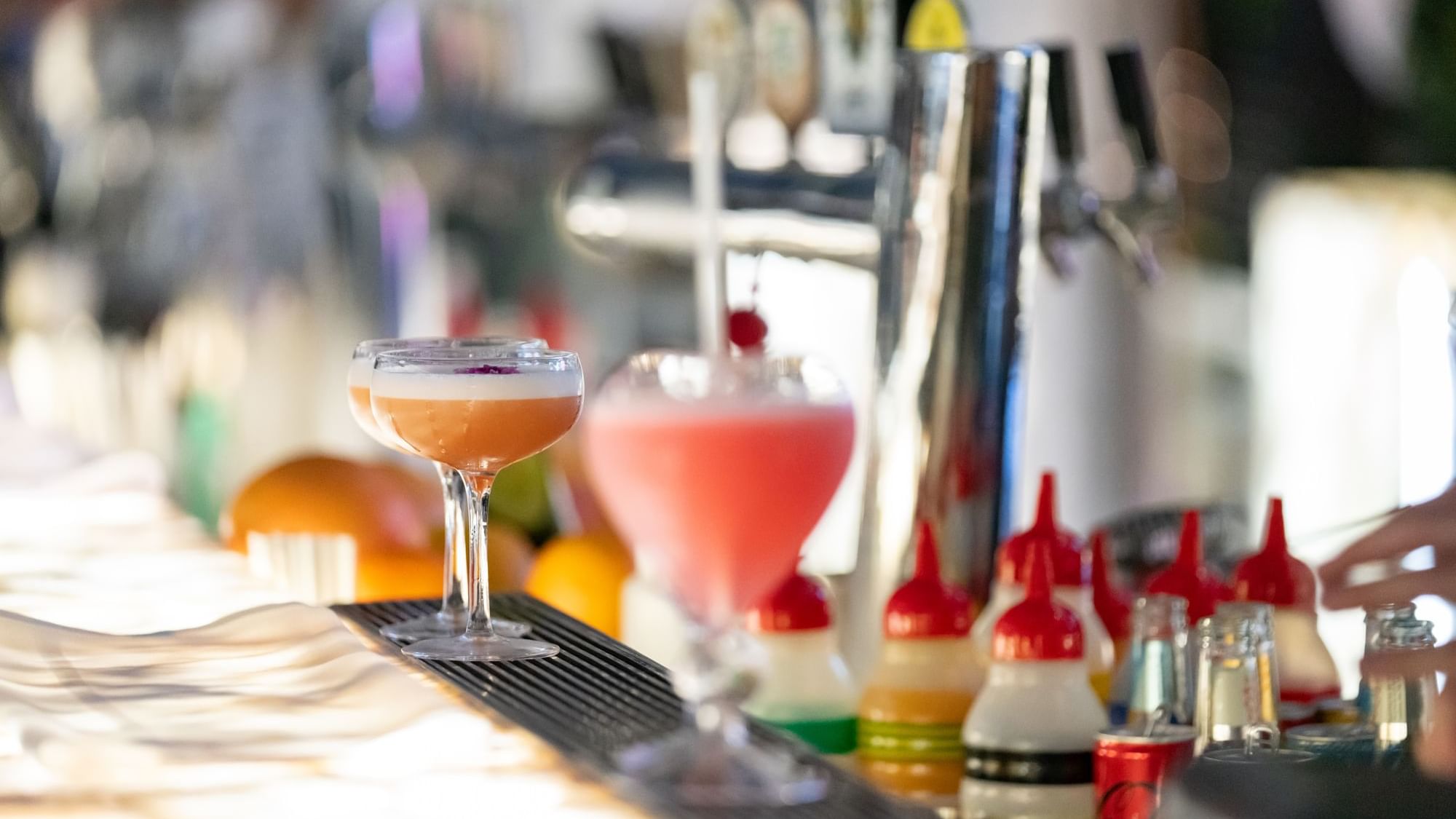 Two cocktails on a bar with a variety of colorful drink mixers and garnishes served at Emporium Hotel South Bank