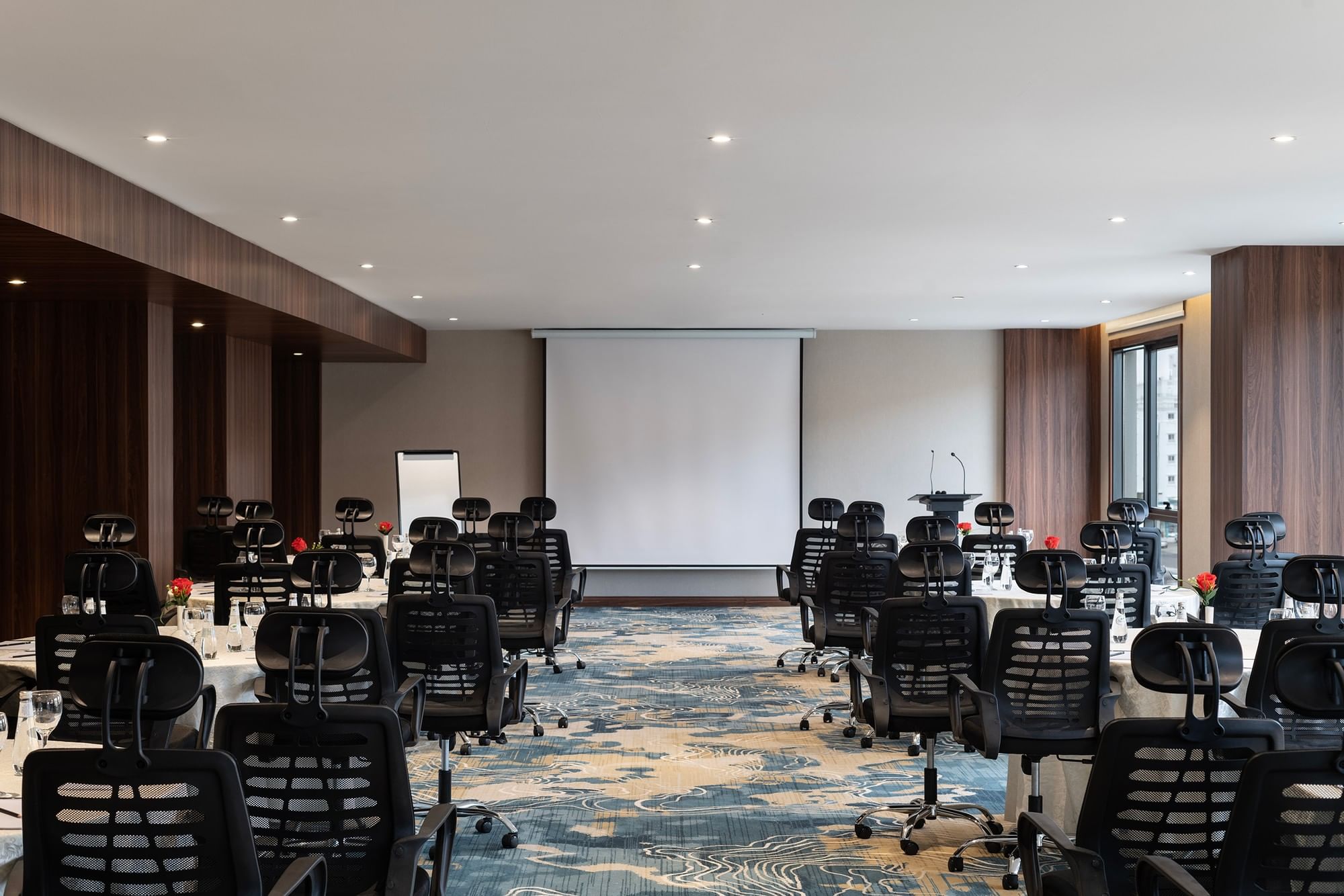 Black office chairs by round tables facing a projector screen in Amarige Hall at Warwick Hotels and Resorts