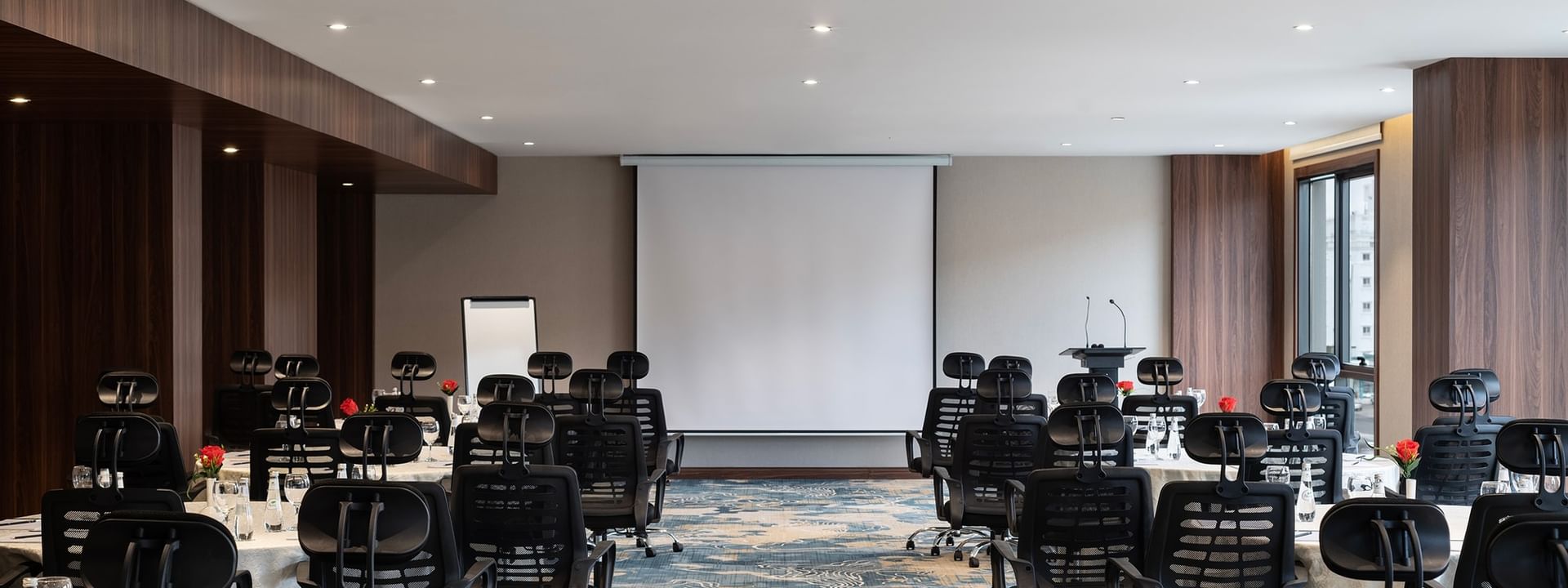 Black office chairs by round tables facing a projector screen in Amarige Hall at Warwick Hotels and Resorts