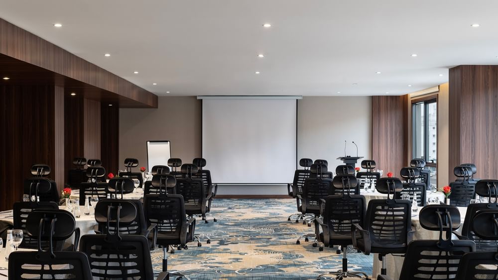 Black office chairs by round tables facing a projector screen in Amarige Hall at Warwick Hotels and Resorts