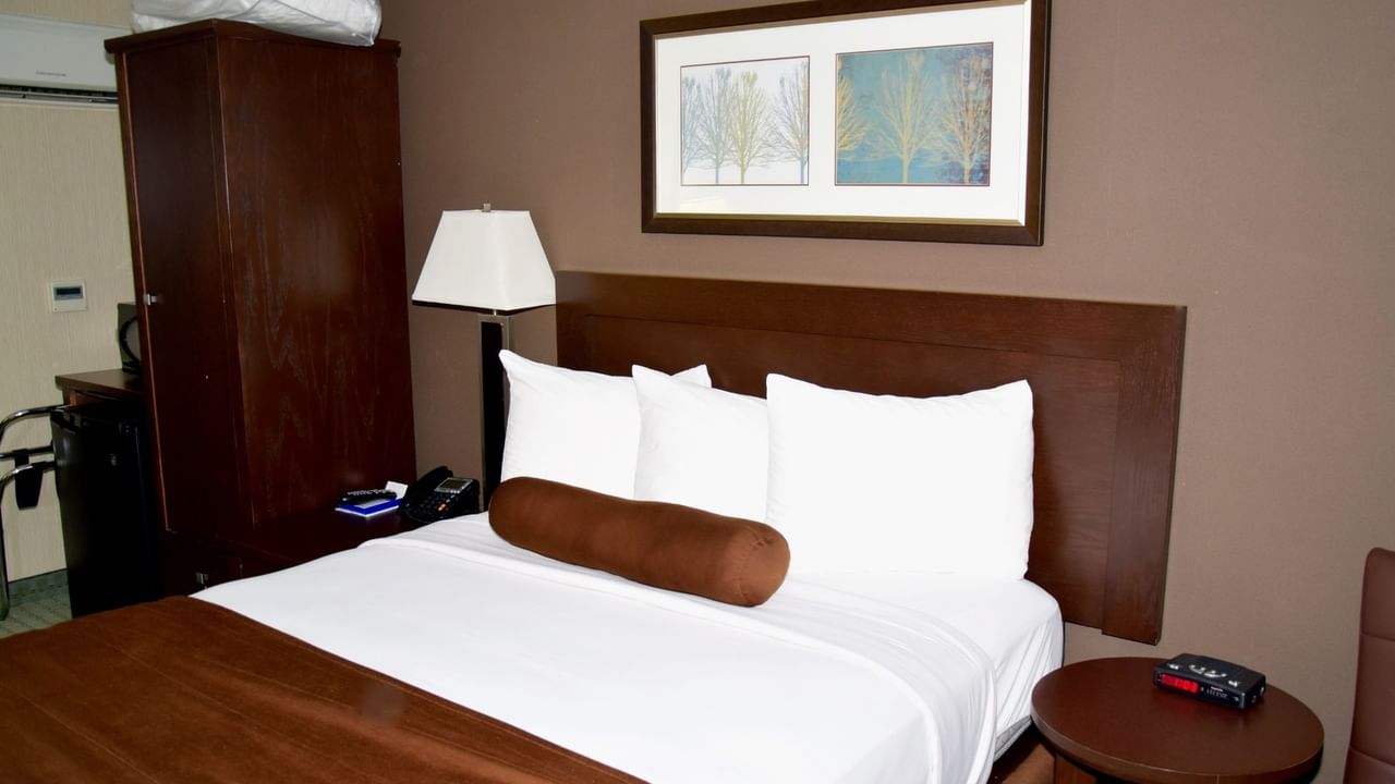 A hotel room with a bed, nightstand, lamp, and framed artwork.